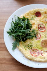 Healthy breakfast in the cafe. Egg omelet with cherry tomatoes decorated with arugula in a white plate on a wooden table. 