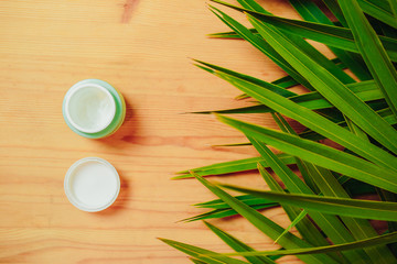 Hand cream with green palm leaves around on the wooden background. Natural flat lay with cream.