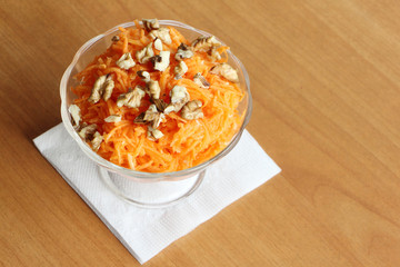 Carrot salad with orange and walnut in a glass plate on a white napkin on a brown background
