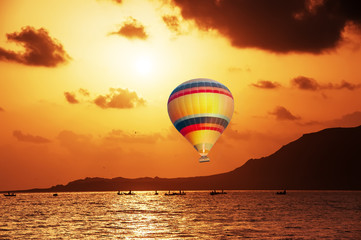 Hot air balloon in the sky above the cliff and the sea at sunset. The atmosphere of relaxation and travel.