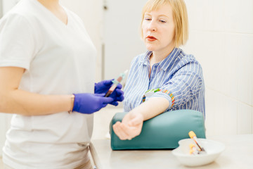 Pensive man is sitting in clinic. Female doctor is doing blood test