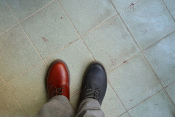 Closeup upper of mismatched shoes, a man wearing two different shoes and different colors standing...