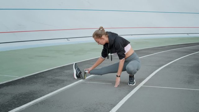 Disabled fit woman stretching legs on track. Lady preparing for workout outdoors
