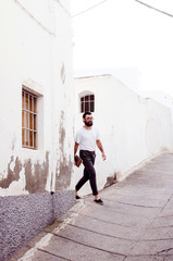 erudite young person with a beard and glasses carries books and walks through the old streets of a town