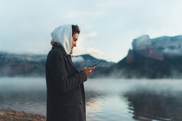 hipster tourist using smartphone trip on foggy lake, mist in mountain nature, traveler girl hold mobile phone, enjoy wifi internet, lifestyle holiday concept