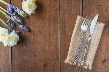 Table setting for spring dinner. Forged fork and knife on burlap napkin, bouquet of white daffodils, blue hyacinths