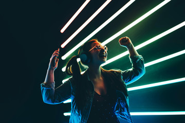Woman in headphones listening music and dancing in neon light.