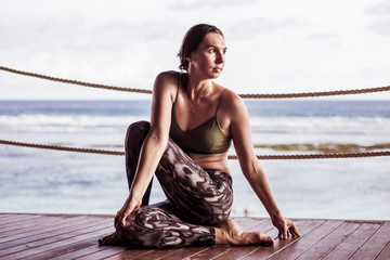 Young caucasian woman practicing yoga, sitting in Ardha Matsyendrasana. Half spinal twist pose. Bali, Indonesia