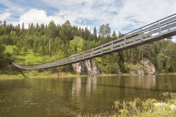Old suspension bridge over the river and two rocks, Ural