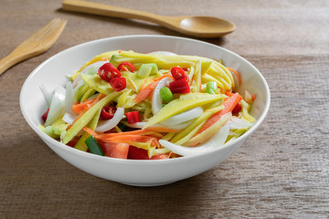 close up of spicy mango salad in a ceramic bowl on wooden table. asian homemade style food concept.
