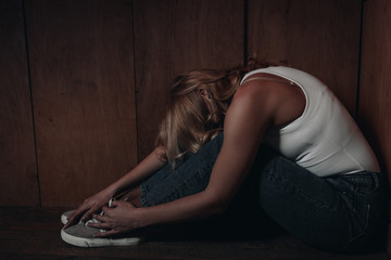 Side view of victim putting head on knees and sitting in corner