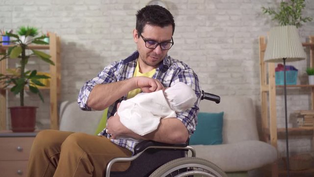 a young father is a disabled man in a wheelchair with a newborn in his hands