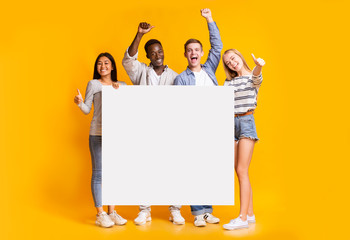 Positive group of teenagers standing together with white placard - obrazy, fototapety, plakaty