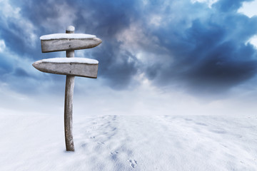Wooden Signpost on Winter Backdrop. Field Covered with Snow on Foreground and Clouds on Background