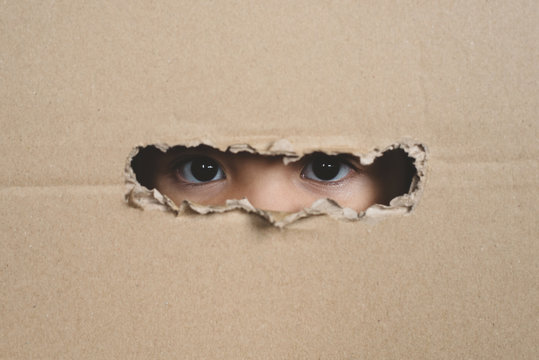 A child eye looking through a hole on a cardboard box. Concept of spy and stalker