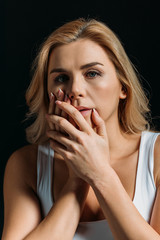 Woman touching face with bruise and looking at camera isolated on black