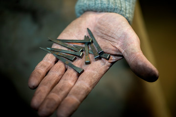 Close-up a dirty blacksmith's hand holds a nails for horseshoe