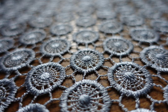 Macro of silver gray crochet lacy fabric on wood
