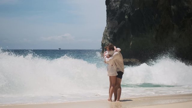 Young romantic couple hugging on empty tropical beach with blue ocean. Attractive couple on paradise island. Touching moment of couple getting engaged