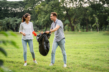 Fototapeta premium Volunteer lovers couple wearing gloves walking to to pick up garbage in the park To keep the environment clean