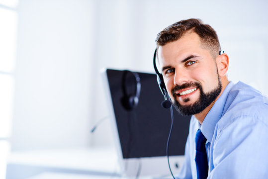 Handsome support man smiling and working with headset and computer in office