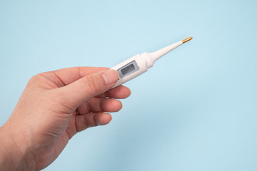 A male hand holding a digital thermometer in hand on a blue background.