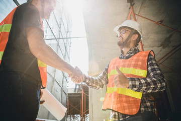 Hanshake seals an agreement at construction site. Architect and worker handshaking on construction site. building, teamwork, partnership, gesture and people concept.