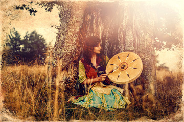 beautiful shamanic girl playing on shaman frame drum in the nature, old photo effect.