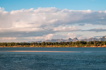 Fototapeta premium A small sand dune in the middle of the Mekong River with a view of Laos mountain scenery