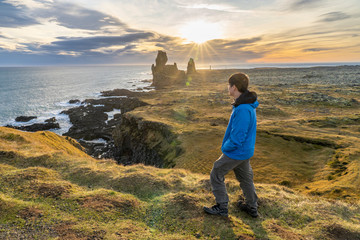 Young asia man standing to see sunset (Sunstar effect) in afternoon at volcanic rock  coast at  Londrangar famous cliffs in west iceland horizontal image