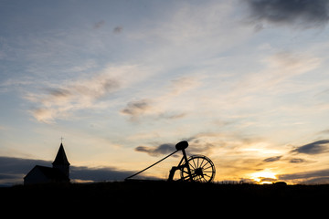 Silhouette Church of Hellnar with Old Haymaking Machine (tractor) on grass field sunset time