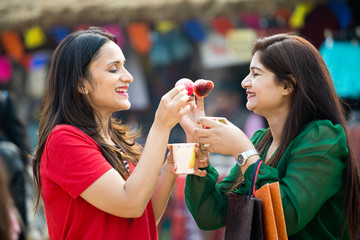 Two women eating flavored ice gola dipped in syrup