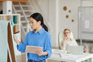 Obraz premium Side view portrait of Asian businesswoman writing on whiteboard while planning project in office, copy space