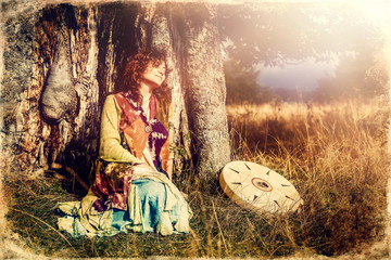 beautiful shamanic girl playing on shaman frame drum in the nature, old photo effect.