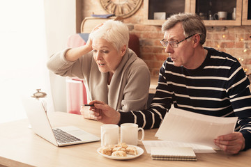 Fototapeta na wymiar Concerned Senior Couple Using Laptop In Kitchen, Managing Family Budget