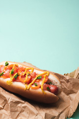 yummy hot dog with mustard in paper on blue