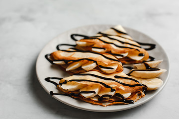 Pancakes with banana, chocolate and raspberries on a plate on a light concrete background. The view from the top.  side view. space for text