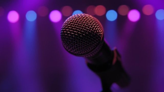 Close-up of microphone on stage in the dark against the background of multicolored lights of concert lighting. Slow motion.