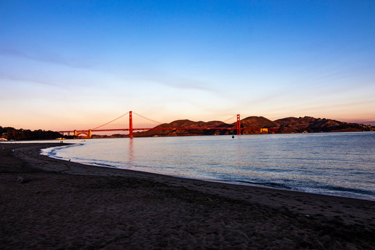 Sunset over San Francisco Bay, California with the red Golden Gate Bridge and mountains in the background and wave and light reflecting in the water in the foreground, horizontal image