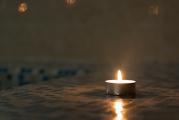 Burning candle in the dark on a swimming pool background.
