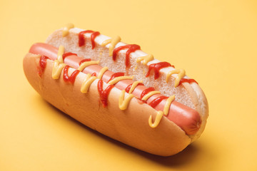close up of tasty hot dog with sausage, mustard and ketchup on yellow