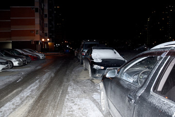 Cars are parked on the site near the house. On the street night, winter, cars covered with snow.