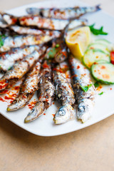 Fresh Grilled sardines served with fresh tomatoes, cucumbers slices and lemon on white plate for mediterranean healthy meal