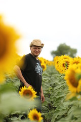  young man in a beige hat and a black t-shirt in a field where sunflowers with a bouquet enjoy the summer landscape
