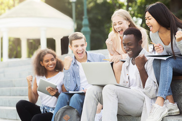 Group of multiracial students celebrating success, checking exam results online
