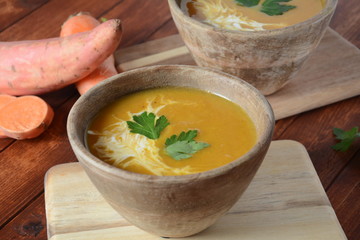 Sweet potato and carrot soup served with sour cream in wooden bowl. Orange vegetable soup concept. Vegan food