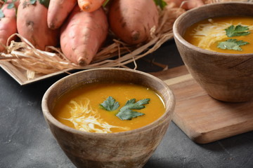 Sweet potato and carrot soup served with sour cream in wooden bowl. Orange vegetable soup concept. Vegan food