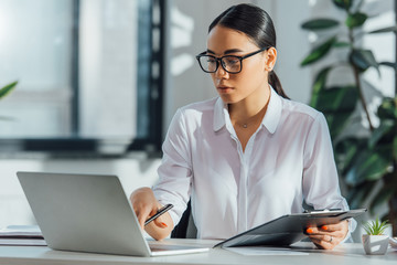asian translator in eyeglasses working online with laptop in office