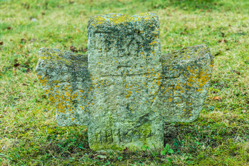 The alone ancient christian tomb cross  with runes covered with moss and lichen among green grass...
