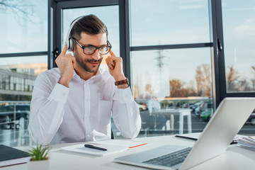 professional male translator in eyeglasses working online with headphones and laptop